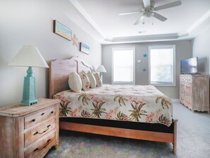 Ein Schlafzimmer mit Bett, Schminktisch, Deckenventilator und zwei Fenstern.