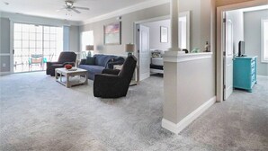 Ein geräumiges Wohnzimmer mit Deckenventilator, einer Couch, einem Couchtisch und Blick durch eine Glastür zu einem Außenbereich.