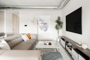 Ein modernes Wohnzimmer mit einer Couch, einem Couchtisch und einem großen, an der Wand montierten Flachbildfernseher.