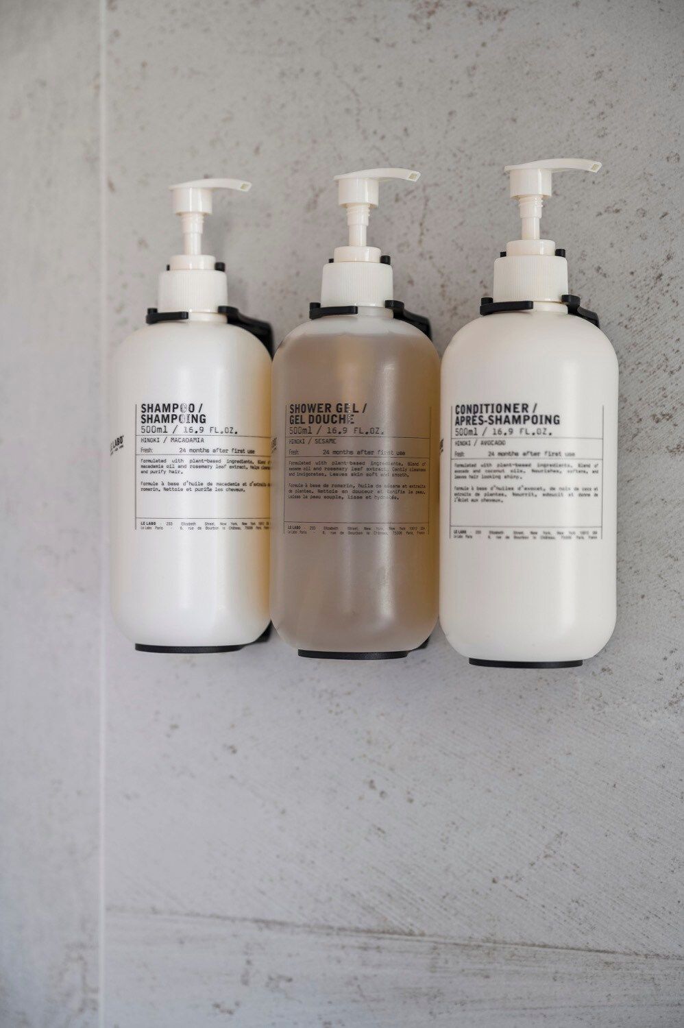 Tres botellas de productos líquidos con dispensadores, etiquetadas como champú, gel de ducha y acondicionador.