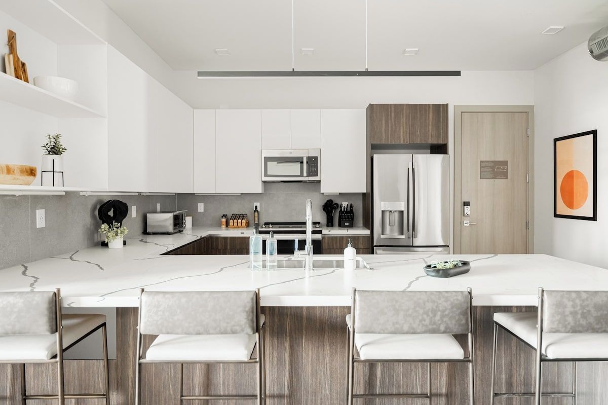 A modern kitchen with white cabinetry, a central island with bar stools, and a microwave above the island.