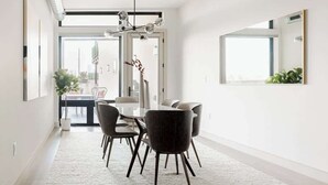 Een moderne eethoek met een glazen tafel, donkere stoelen en een kroonluchter.