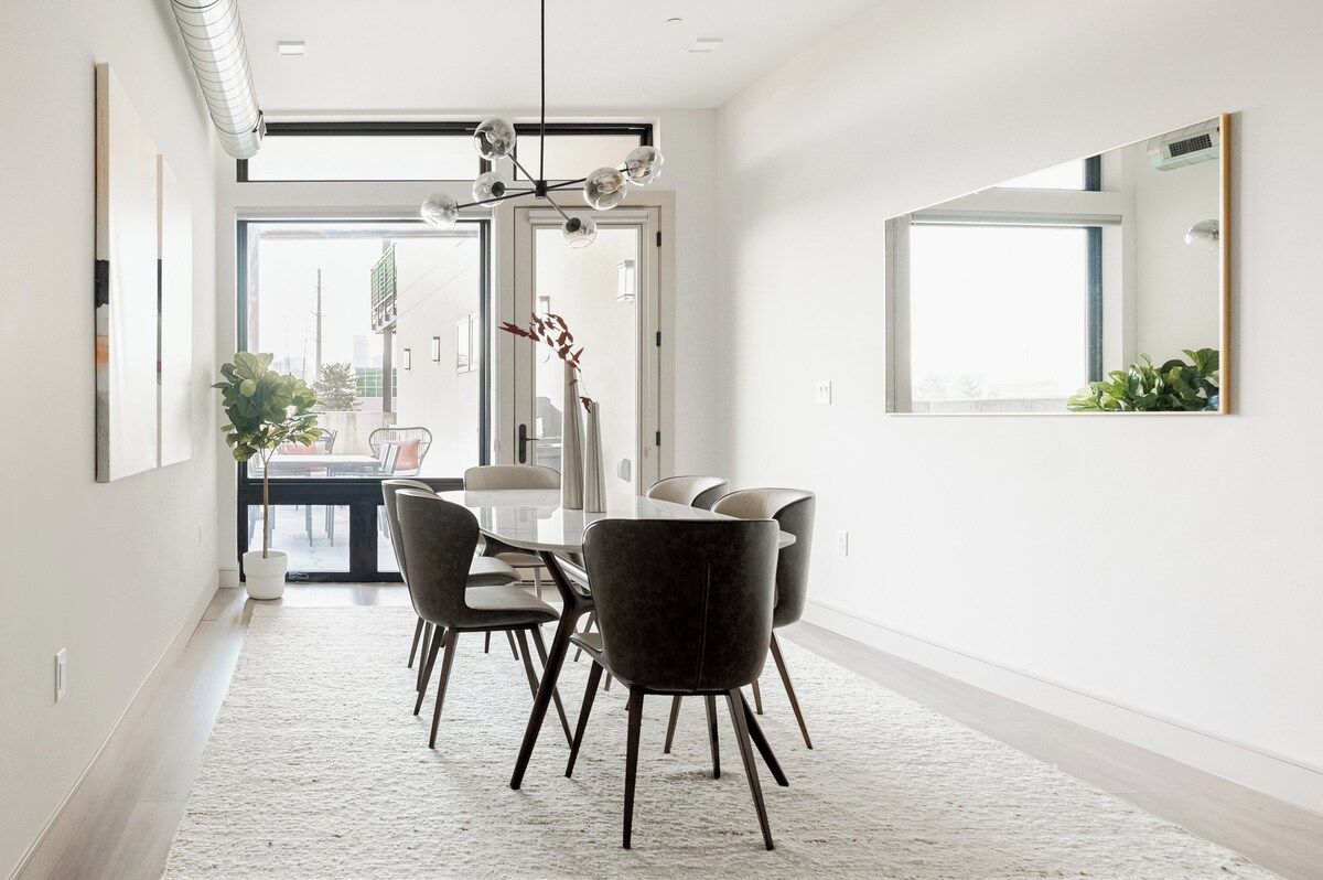 A modern dining area with a glass table, dark chairs, and a white rug.