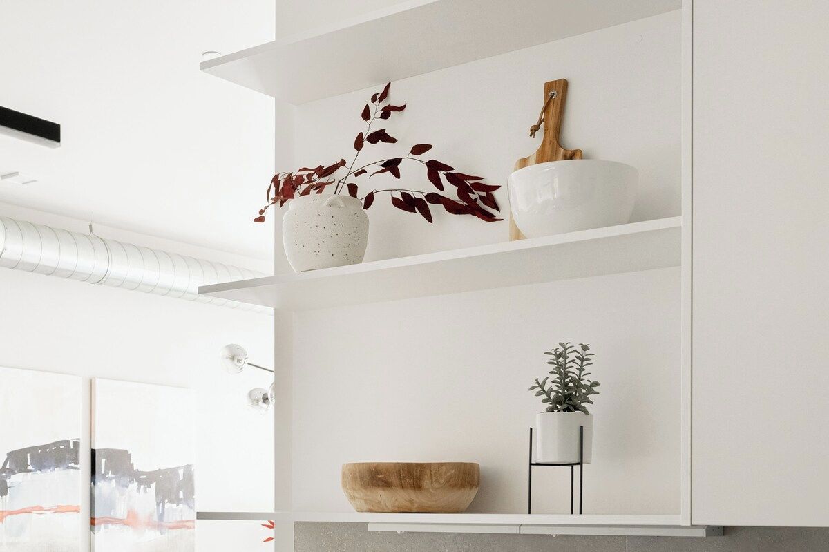 A modern kitchen with white cabinetry, a wooden bowl on the countertop, and a potted plant on a stand.