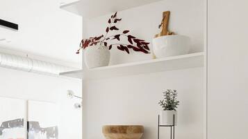 A modern kitchen with white cabinetry, a wooden bowl on the countertop, and a potted plant on a stand.