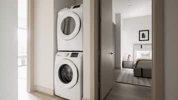 A laundry room with two stacked washing machines and a bedroom with a bed and nightstand.