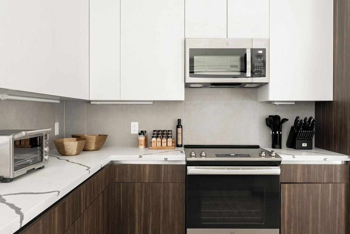 Una cocina moderna con microondas integrado, horno y tostadora. Hay cestas de madera y recipientes para especias en la encimera.