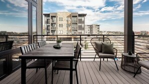 A balcony with a wooden table and chairs, a potted plant, and a view of modern buildings. - Modern Penthouse | Private Skyline Balcony (Denver)
