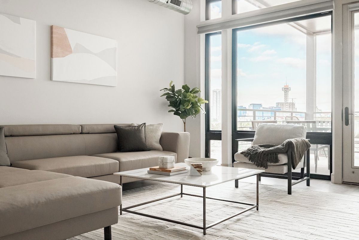 A modern living room with a sofa, coffee table, and a view of the city through large windows.