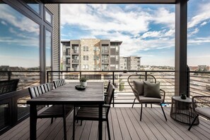 Een balkon met een houten tafel en stoelen, met uitzicht op een stadsgezicht met moderne gebouwen.