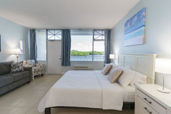 Un dormitorio con cama, sofá, mesita de noche y ventana con cortinas.