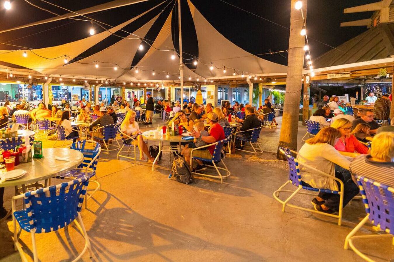 An outdoor dining area with round tables and chairs, under a large canopy.
