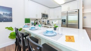 Une cuisine moderne avec des meubles blancs, des appareils en acier inoxydable et un coin repas agrémenté d’assiettes et de chaises bleues.