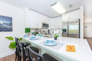A modern kitchen with white cabinets, stainless steel appliances, and a dining area with blue plates and chairs.