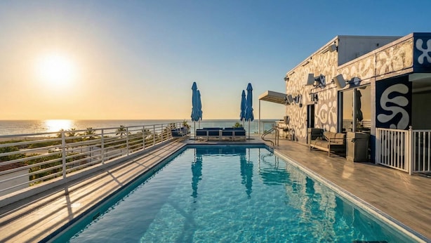 Una piscina sul tetto con acqua cristallina, vista sull'oceano e un edificio con un grande logo a forma di 'S'.