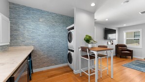 Una cocina moderna con lavadora integrada, un comedor con mesa y sillas, y un amplio ventanal con persianas.