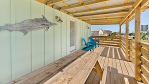 Una terraza de madera con una mesa y sillas, una decoración de pez en la pared y vistas a edificios al fondo.