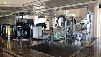 Uma cozinha moderna com pia de aço inoxidável, cafeteira Bosch e diversos eletrodomésticos.