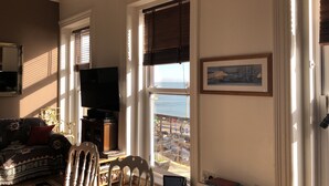 A living room with a television, a dining table, and a view of the sea through large windows. - Apartment - Sleeps 4 - Balcony - Sea View (Eastbourne)