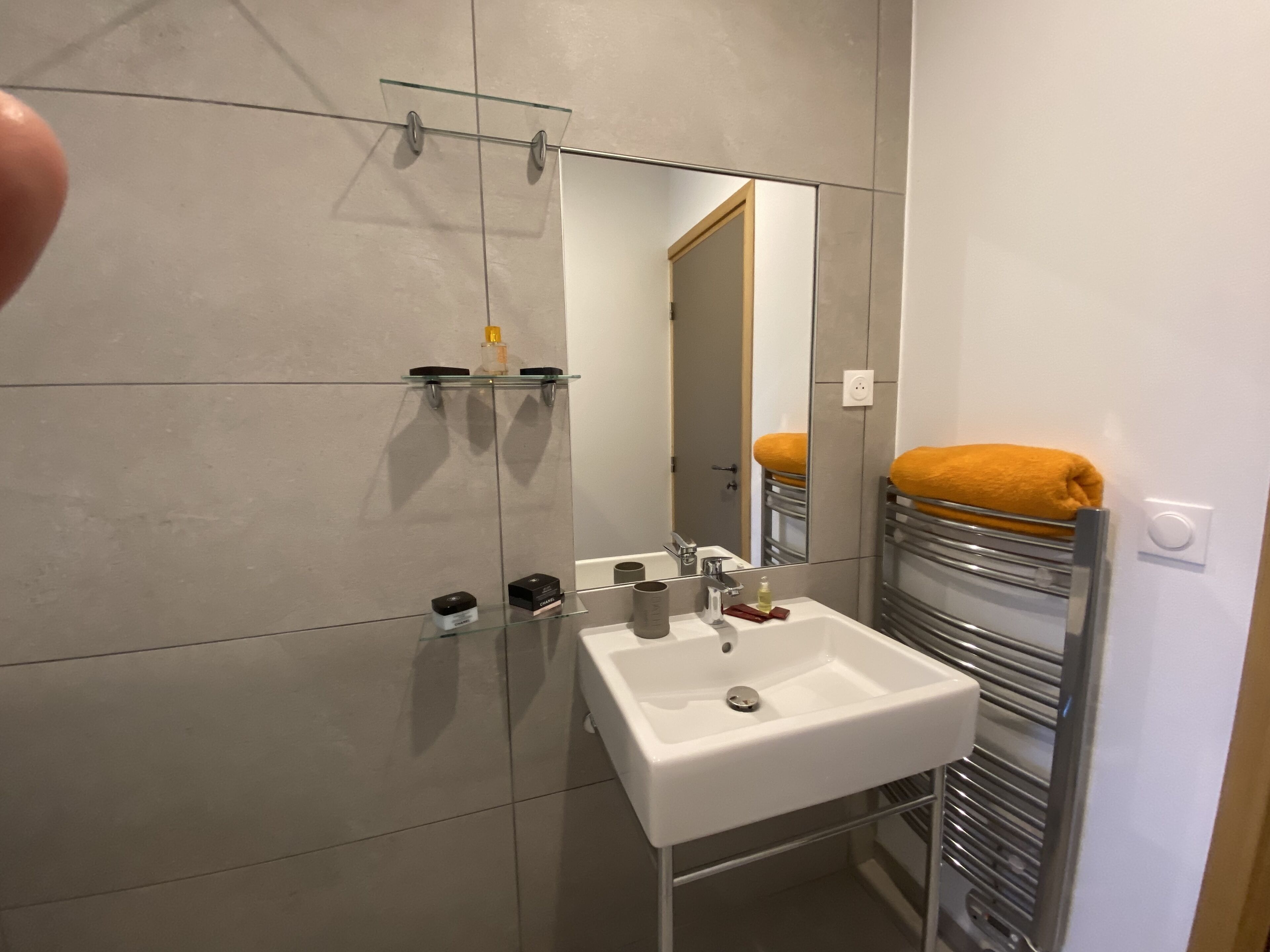 A modern bathroom with a white sink, glass shelves, and a towel rack with an orange towel.