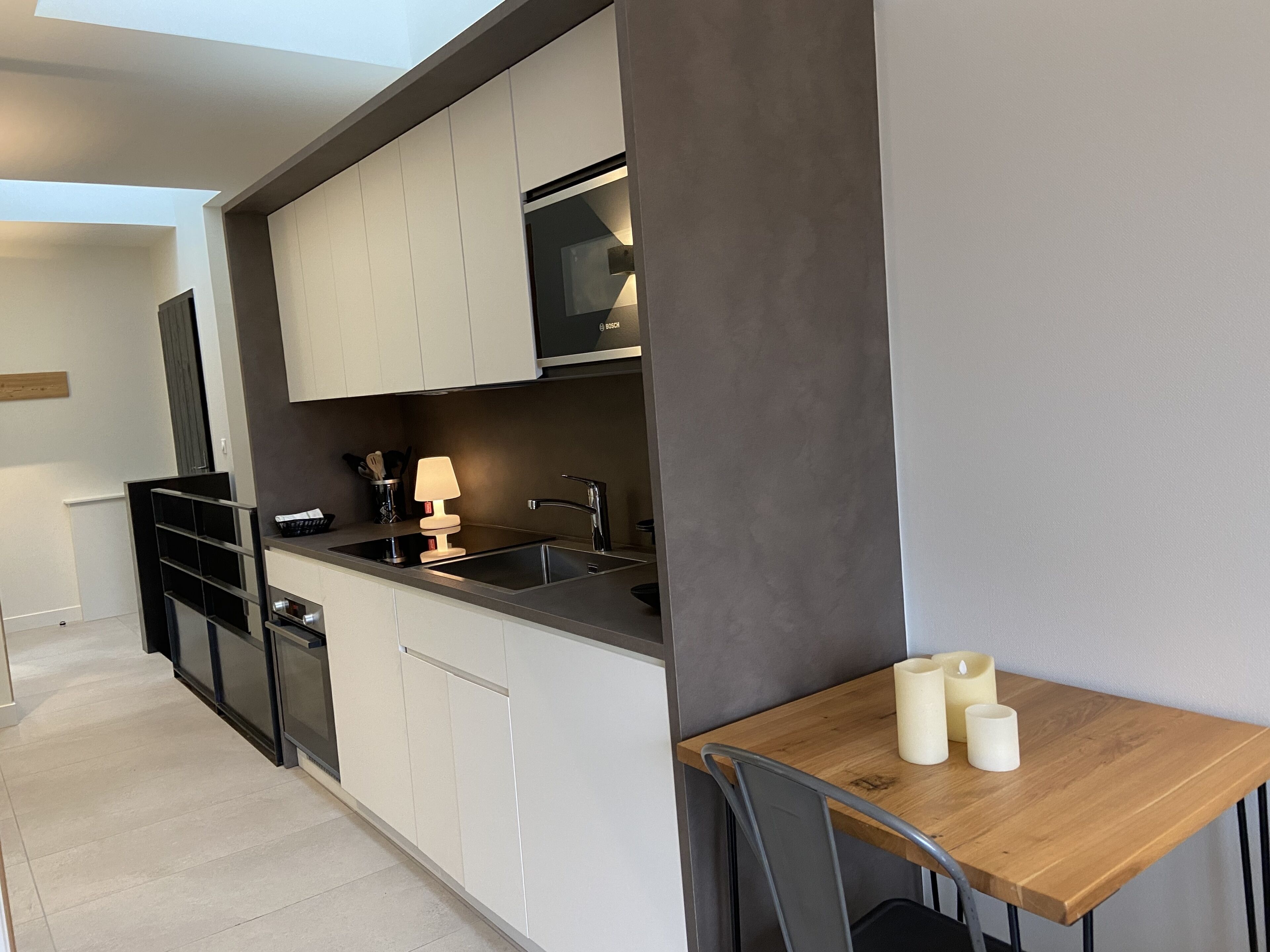 Una cocina moderna con armarios blancos, encimera negra y una mesa de madera con velas.