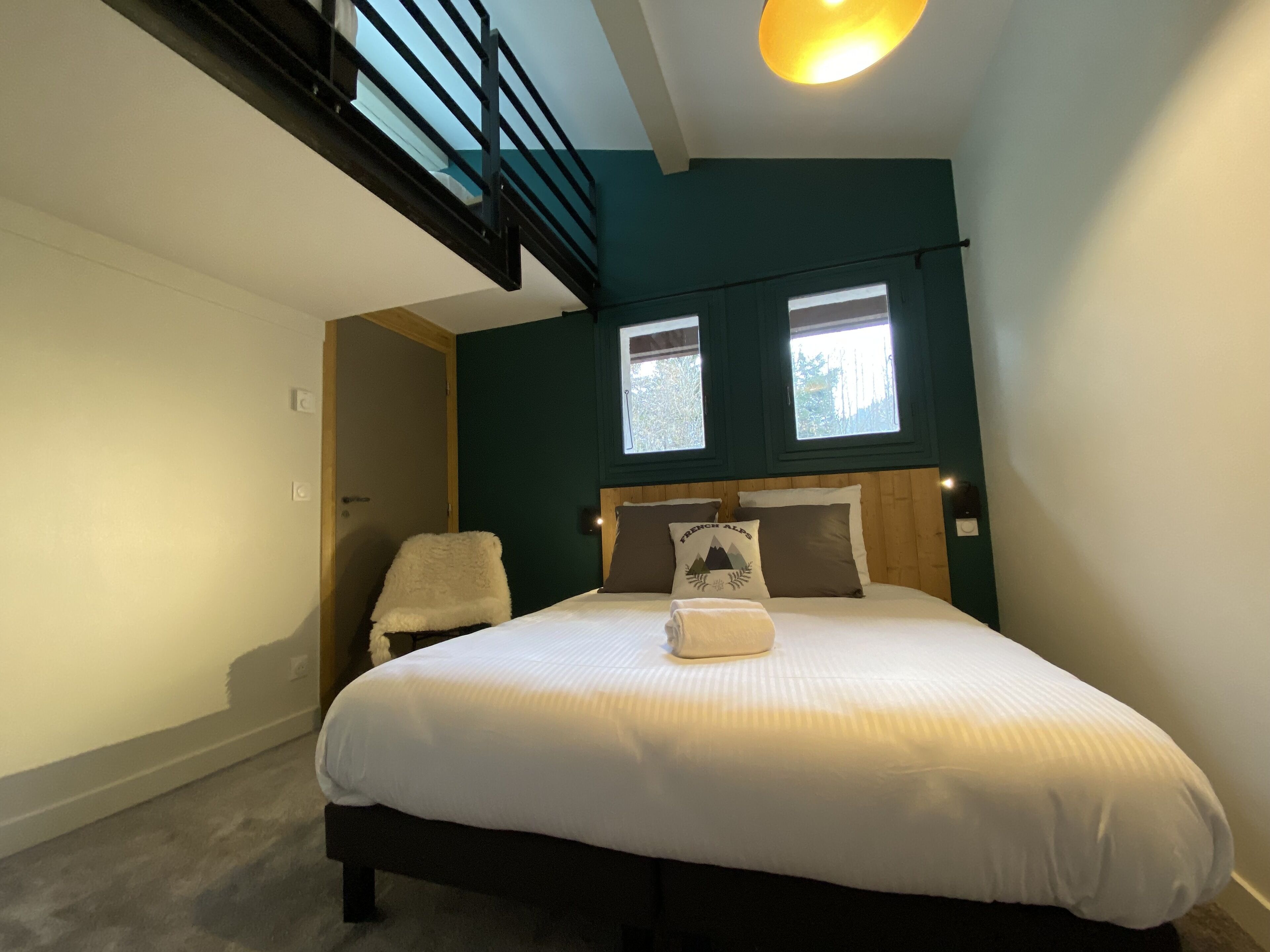 Un dormitorio con cama, una silla, un ventanal y una escalera.