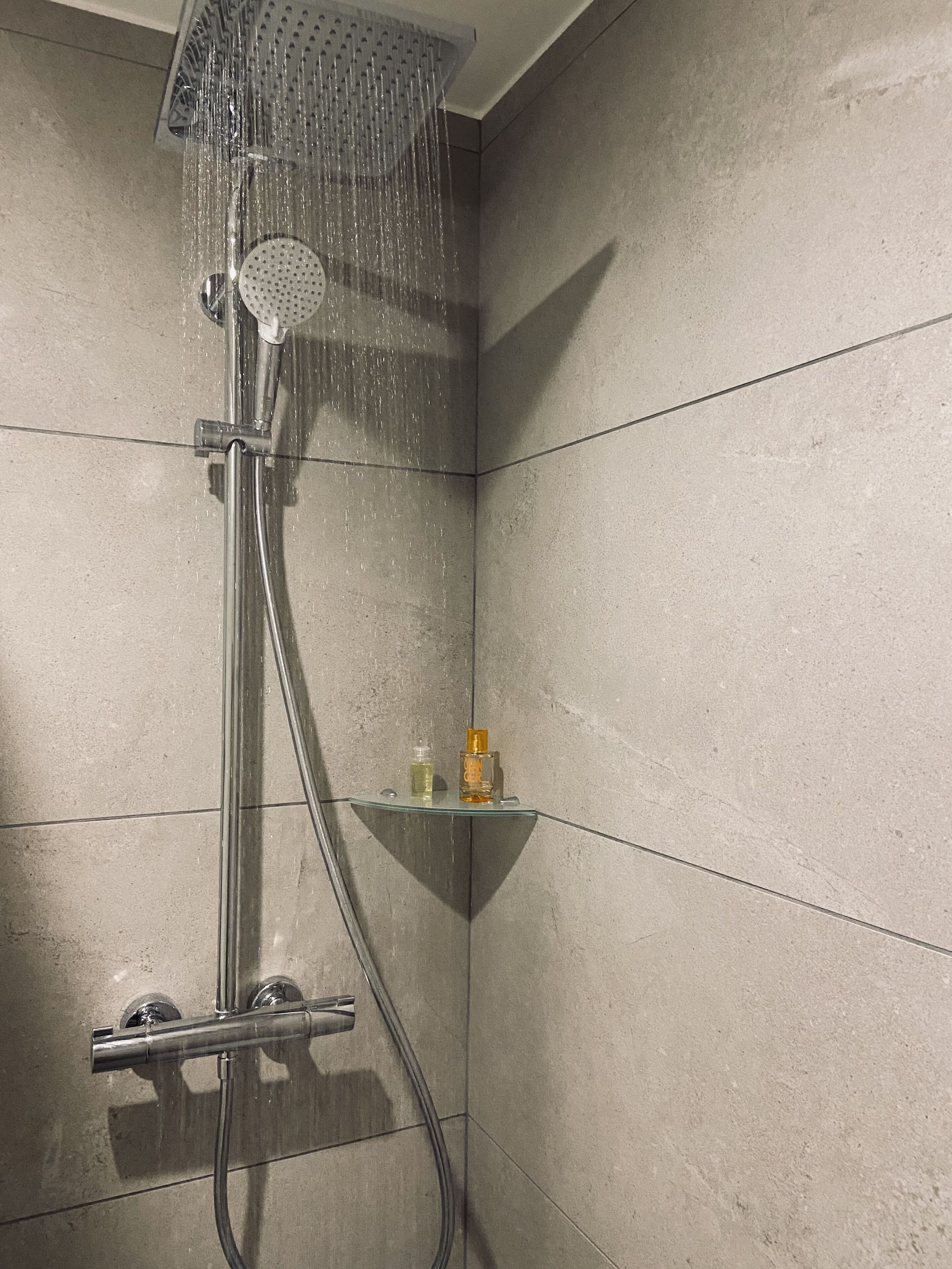 A shower with a glass shelf holding two bottles.