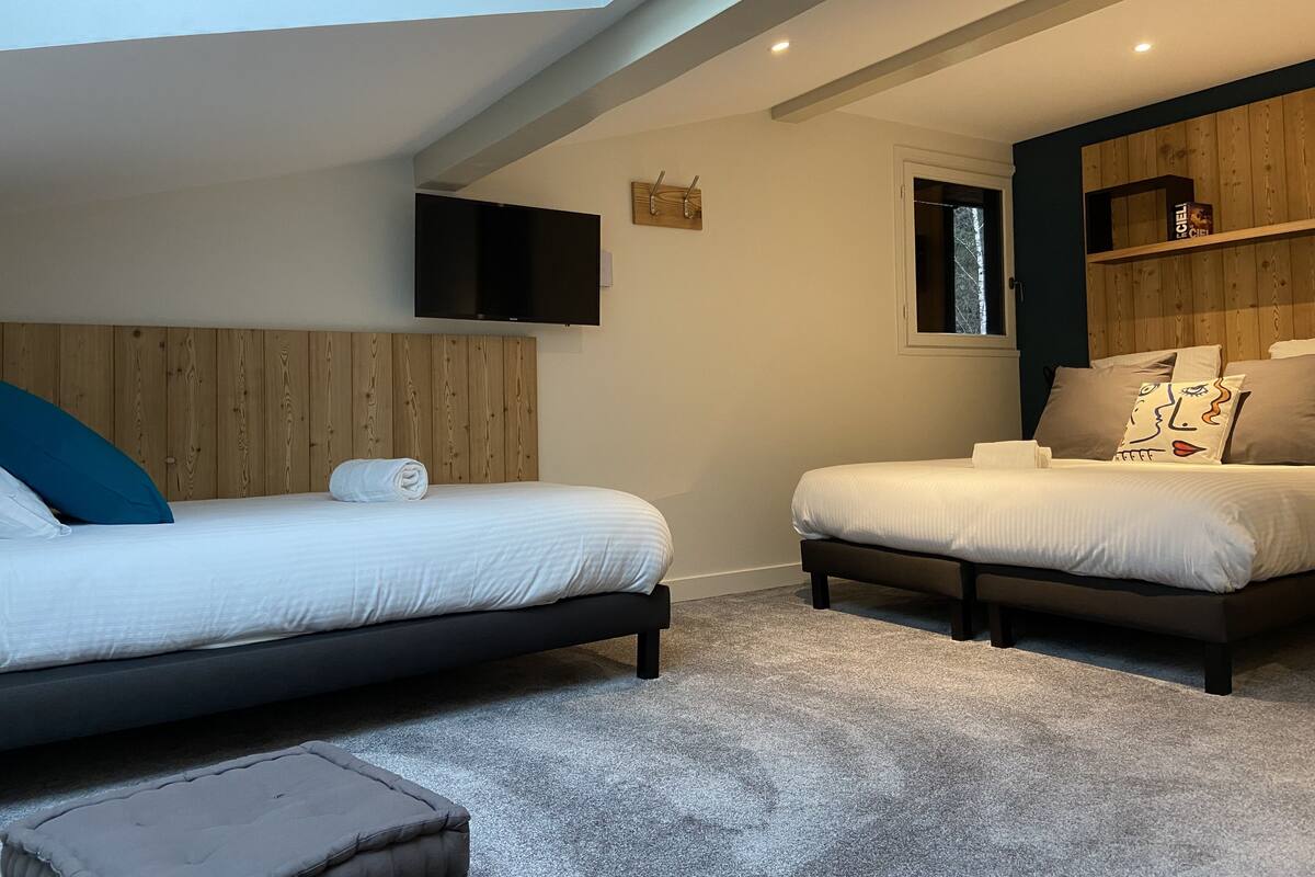 Un dormitorio con dos camas, un televisor montado en la pared y un cabecero de madera.