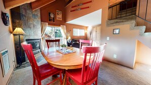 A dining area with a wooden table and red chairs, a fireplace, and a staircase. - Mammoth View Villas 3 Walk to Village Gondola, Cozy Mountain Cabin in Forest Setting by RedAwning (Mammoth Lakes)