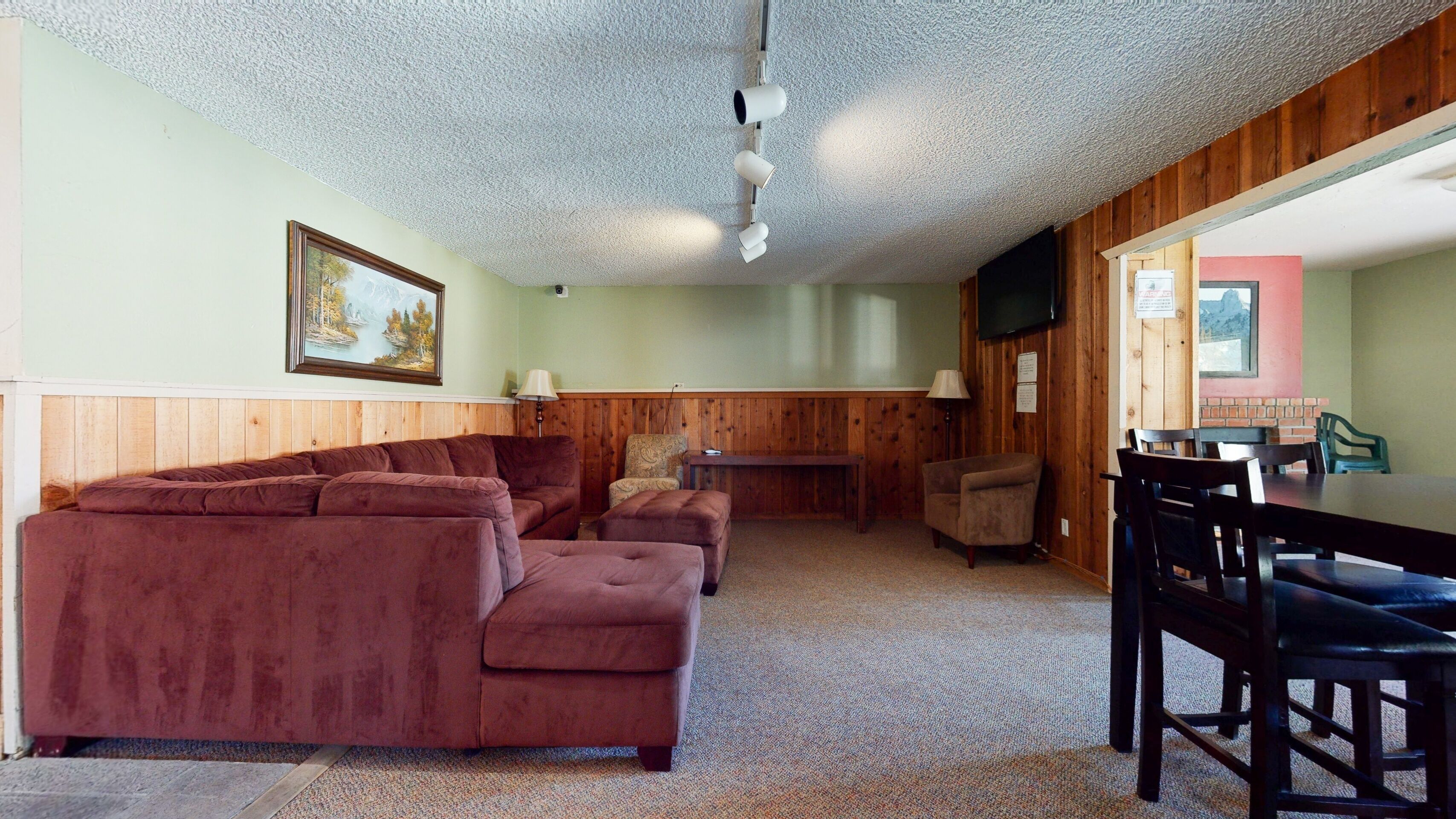 A room with a sectional sofa, a small table, and a television mounted on the wall.