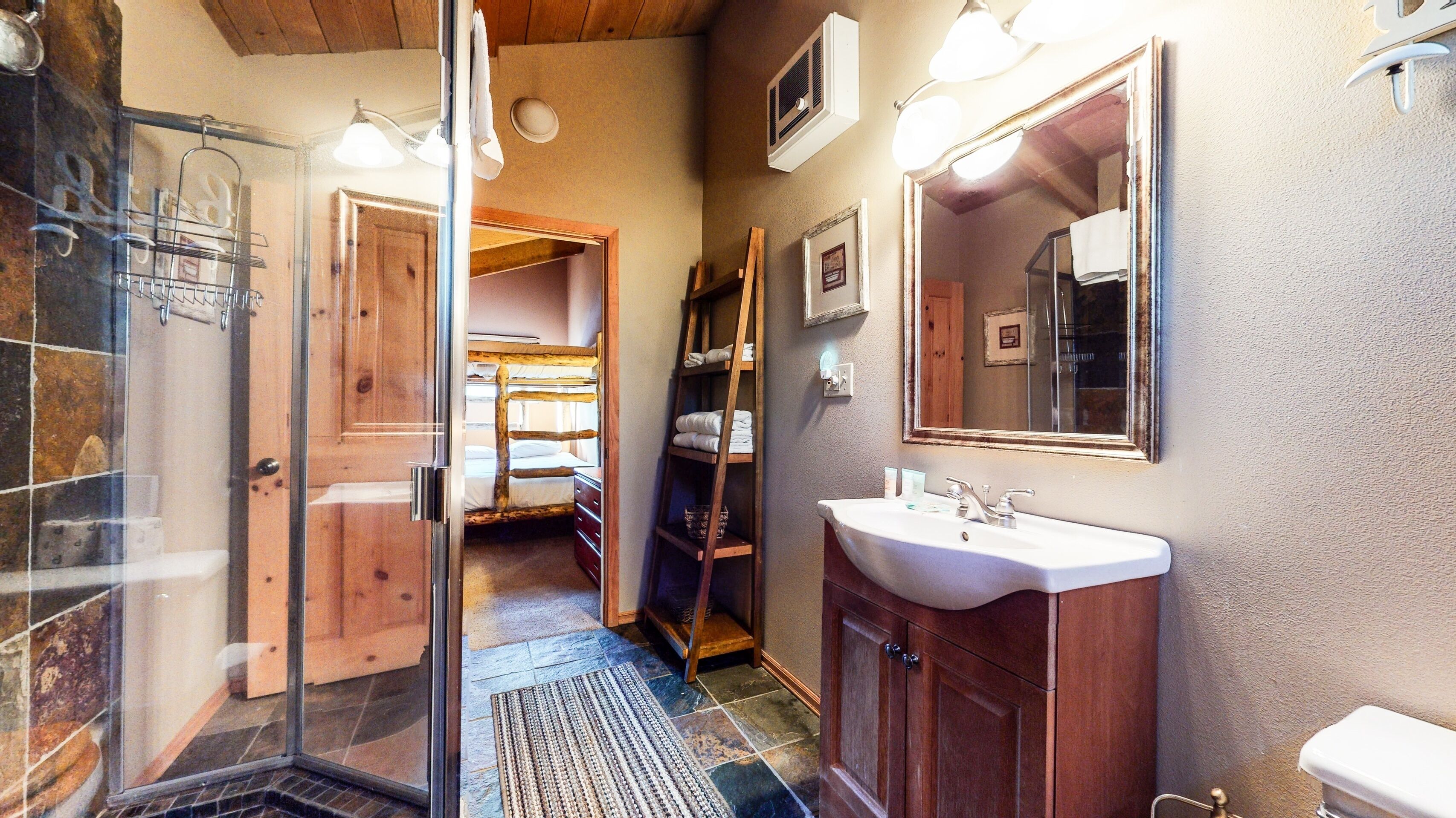 A bathroom with a glass shower enclosure, a wooden ladder shelf, a sink, and a mirror.