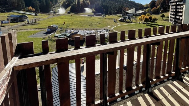 Un balcon en bois offrant une vue sur un paysage montagneux, une gare et un bâtiment à l’architecture moderne.