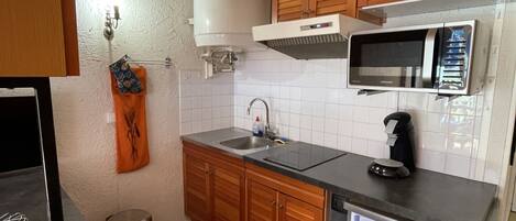 A compact kitchen with wooden cabinets, a microwave, a sink, and a stainless steel refrigerator.