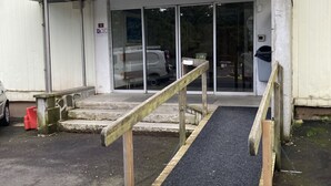 Une entrée d’immeuble avec une rampe menant à une porte, une enseigne au-dessus de la porte et une voiture garée à l’extérieur.