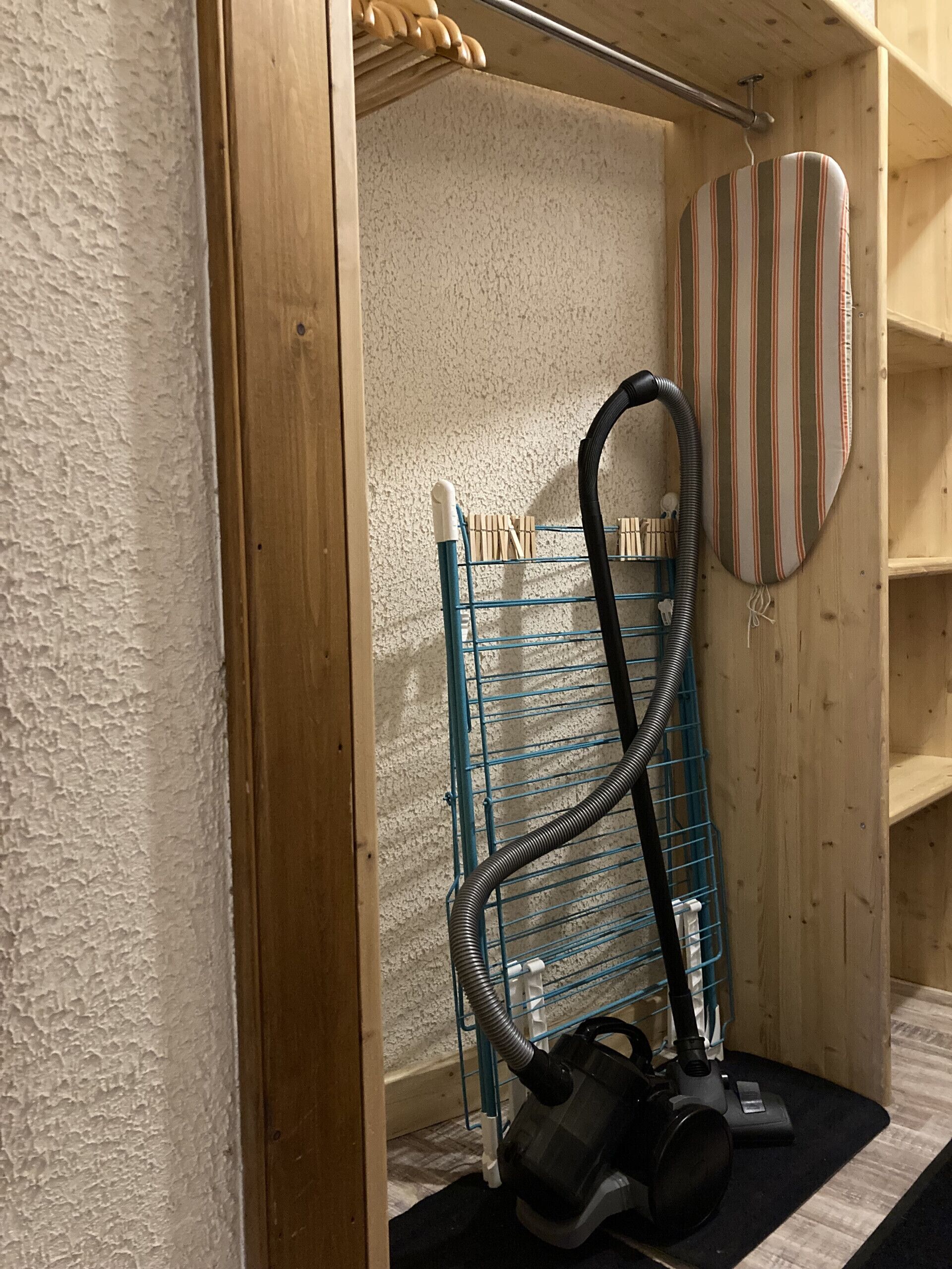 A room with a vacuum cleaner, a striped ironing board, and a blue drying rack.