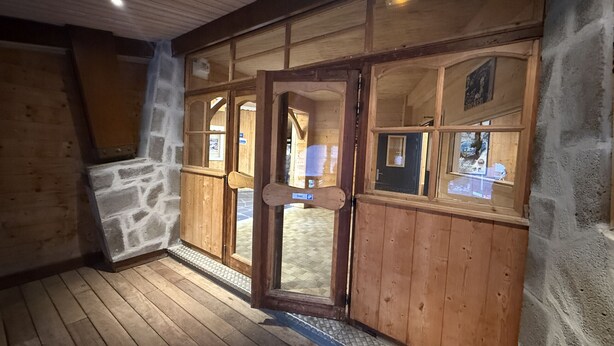 Ein Holzinnenraum mit einer Steinwand, einer Holztür mit Glasfeldern und einem gefliesten Boden.