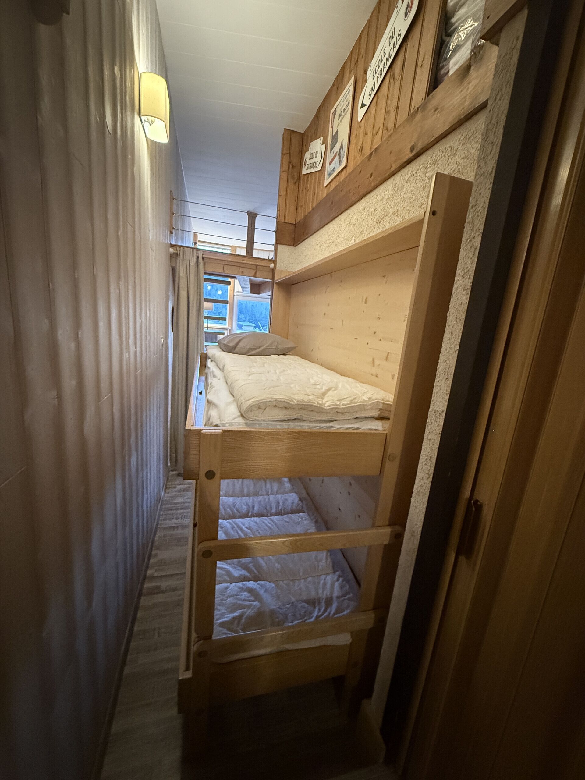 Un corridoio stretto in legno con letti a castello, pareti di legno e una luce a soffitto.
