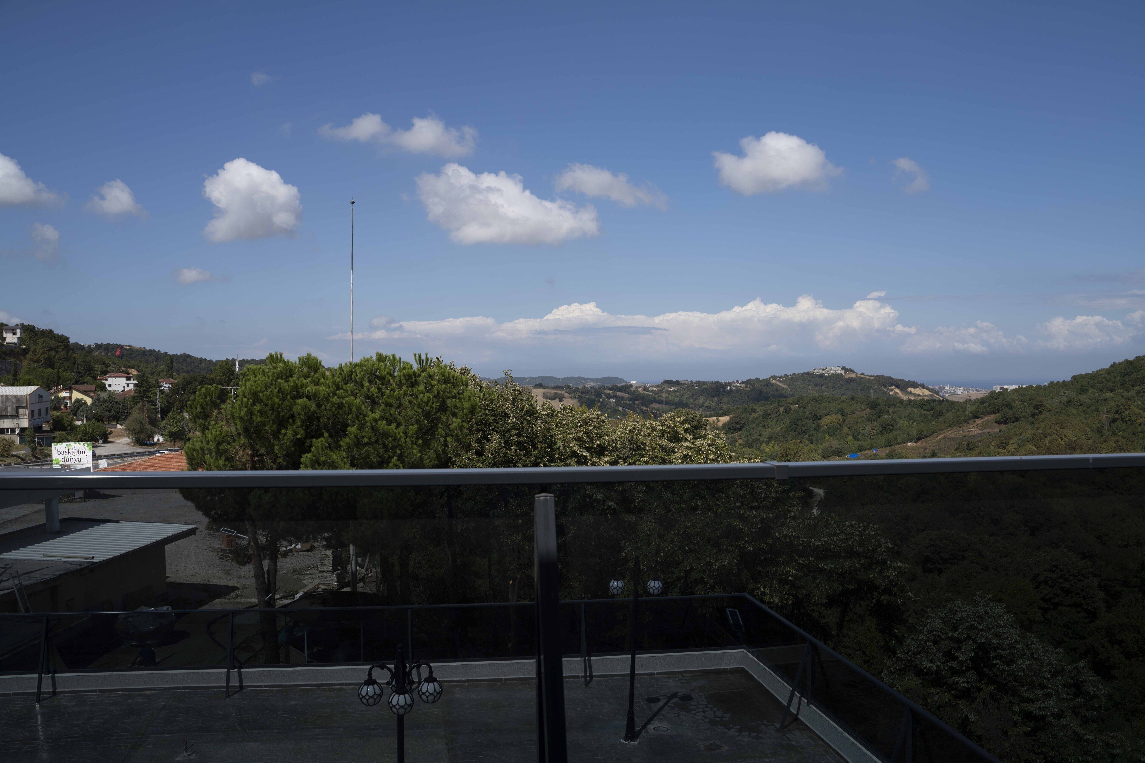 A rooftop terrace with a clear view of a hilly landscape, a flagpole, and a signboard.