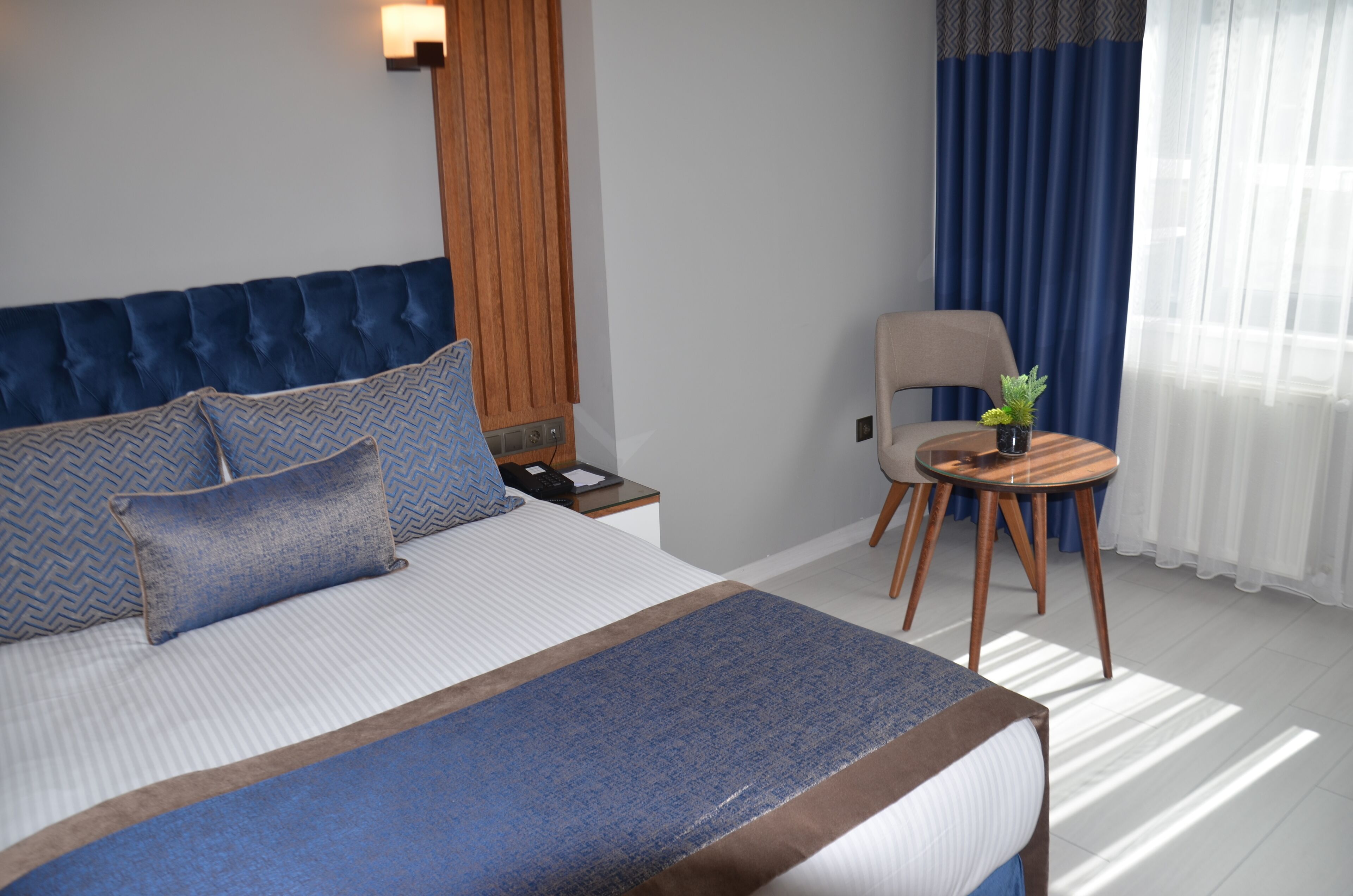 Une chambre d’hôtel avec un grand lit, une table de chevet avec une lampe, une petite table ronde avec une plante et une chaise.