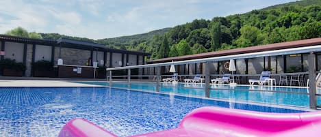 Uma piscina com um escorrega rosa, cadeiras de descanso e um prédio com área coberta.