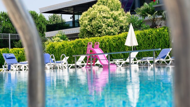 A swimming pool with lounge chairs and a pink slide. - Hotel Vela Verde (Yalova)