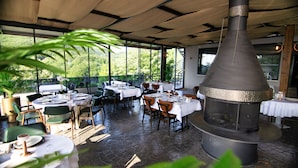 An outdoor dining area with tables set for two, surrounded by chairs, and a large central wood-burning stove. - Hotel Vela Verde (Yalova)