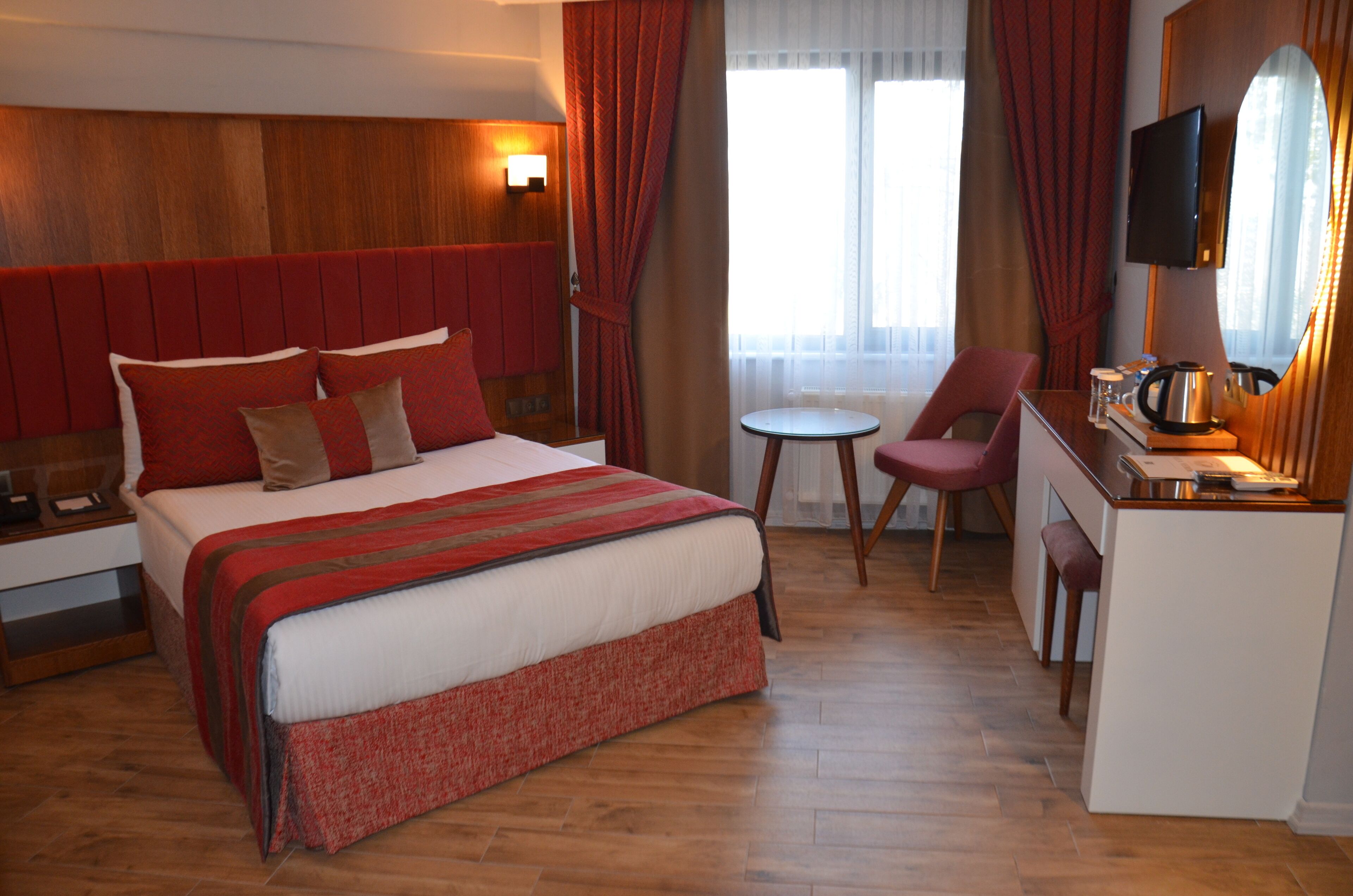 A hotel room with a large bed, a desk with a chair, a small table, and a TV.