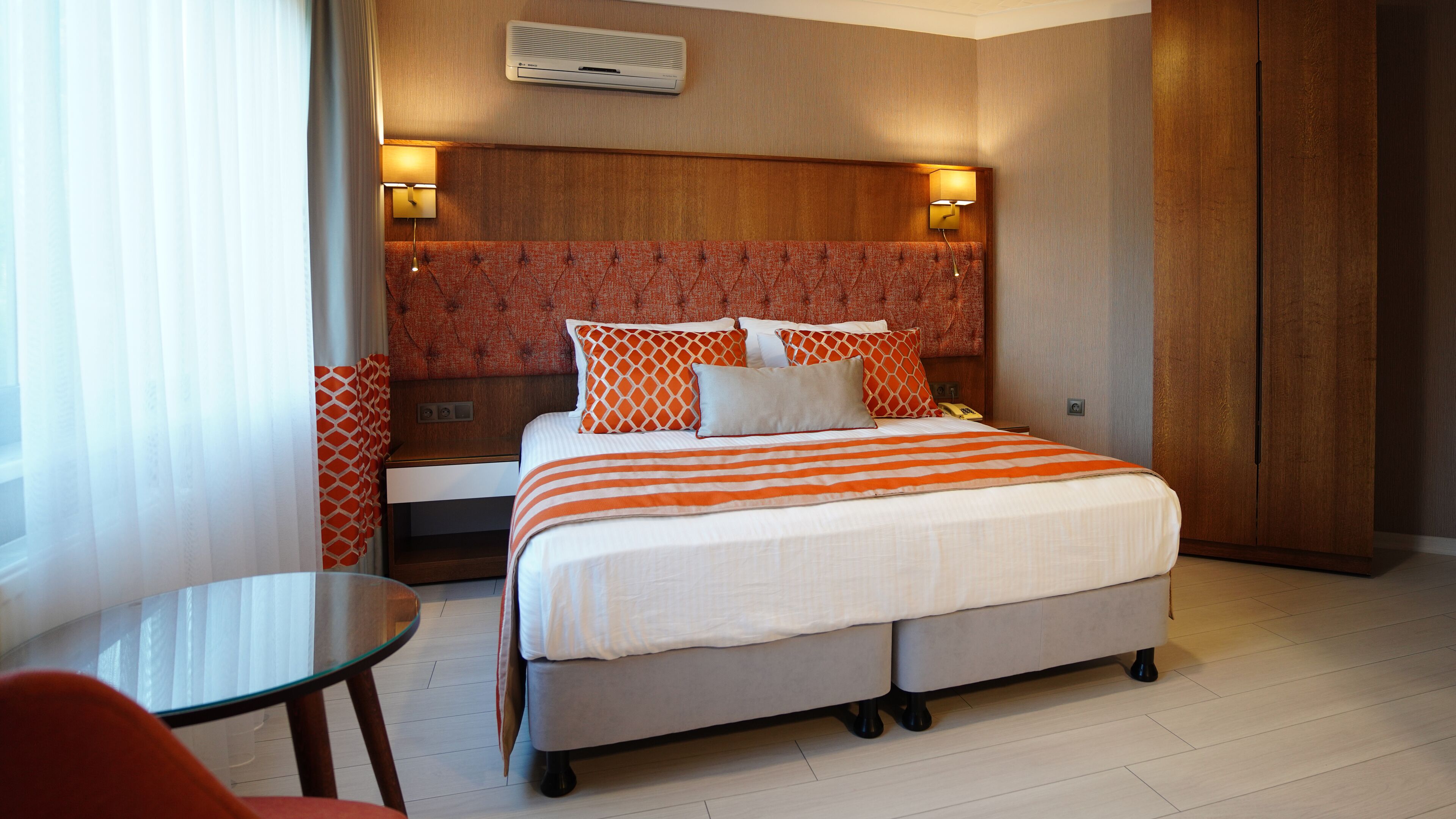 Ein Hotelzimmer mit Bett, Nachttischen, einer Lampe, einem Kleiderschrank und einem kleinen Tisch mit Stuhl.