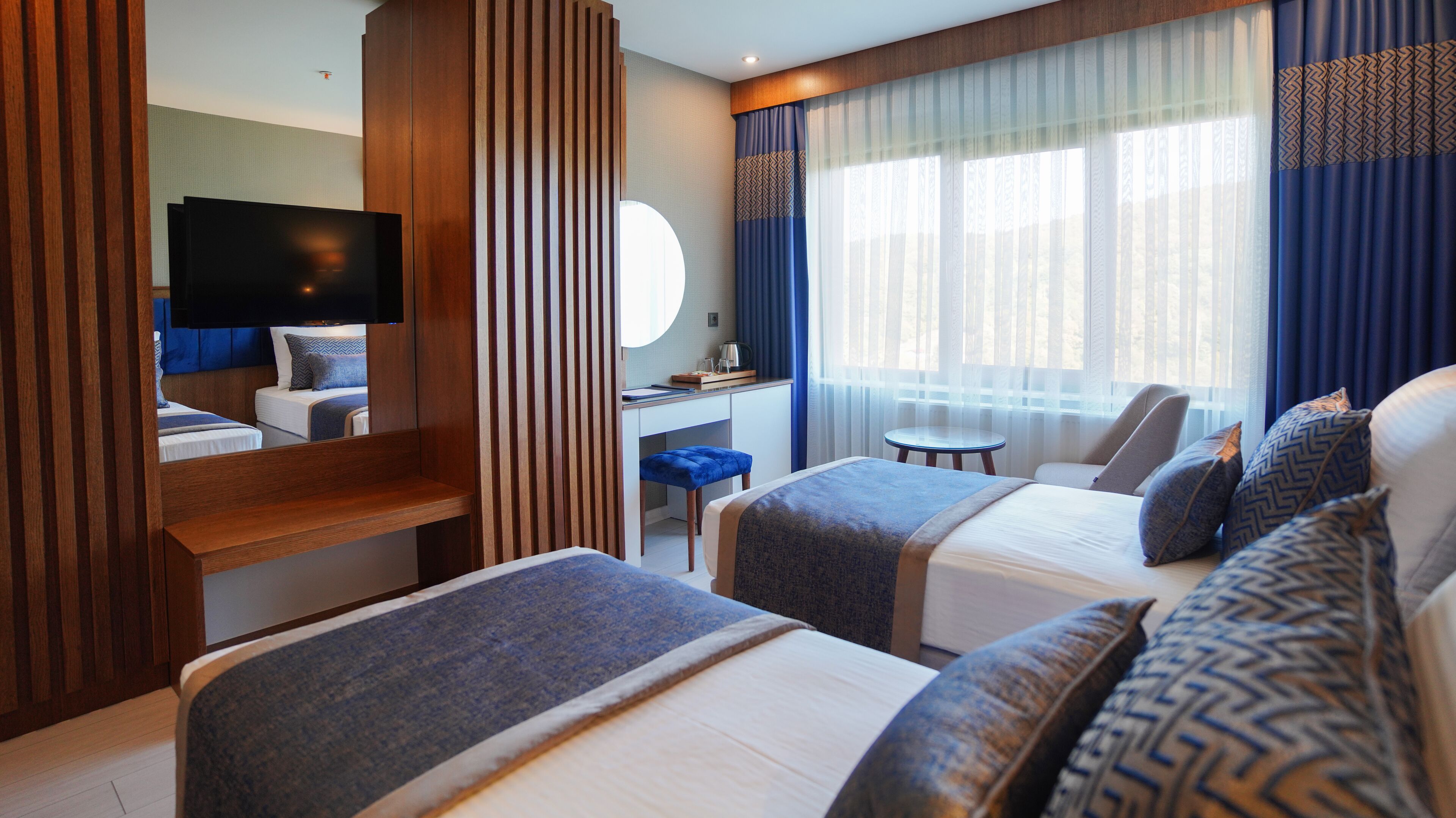 Habitación de hotel con dos camas, un escritorio, una silla, un televisor y una ventana con cortinas.