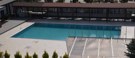 Ein rechteckiger Pool mit Metallgeländer, umgeben von einer gepflasterten Terrasse und einem überdachten Sitzbereich mit Dach.
