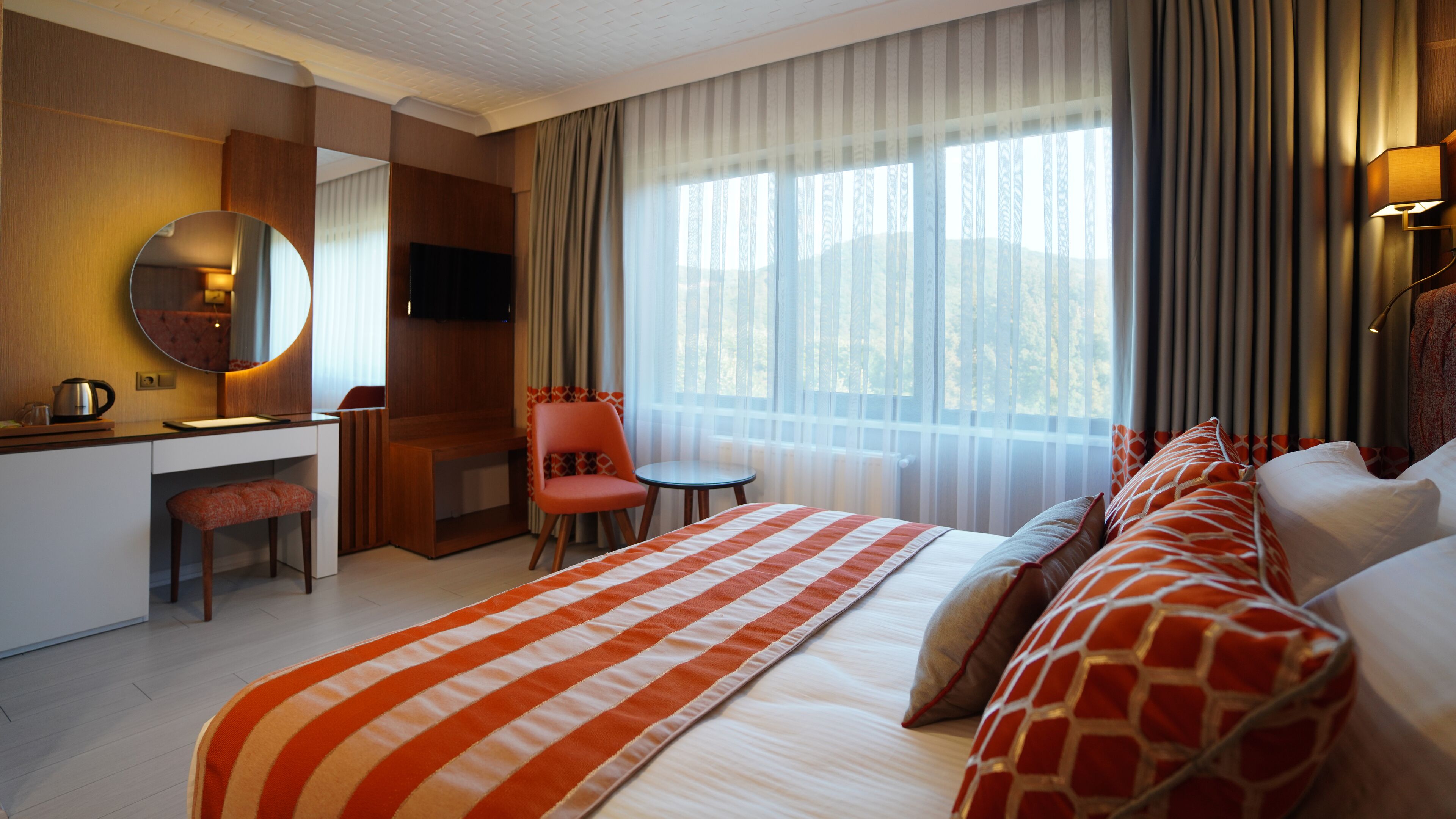 Habitación de hotel con cama, escritorio, silla, televisor y ventana con cortinas.