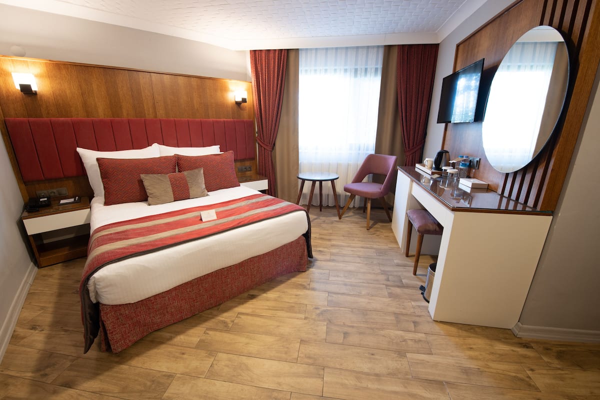 Ett hotellrum med en stor säng, ett skrivbord, en stol, en TV och en spegel.