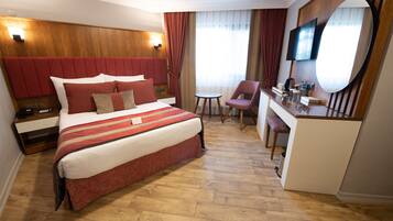 A hotel room with a large bed, a desk, a chair, a TV, and a mirror.