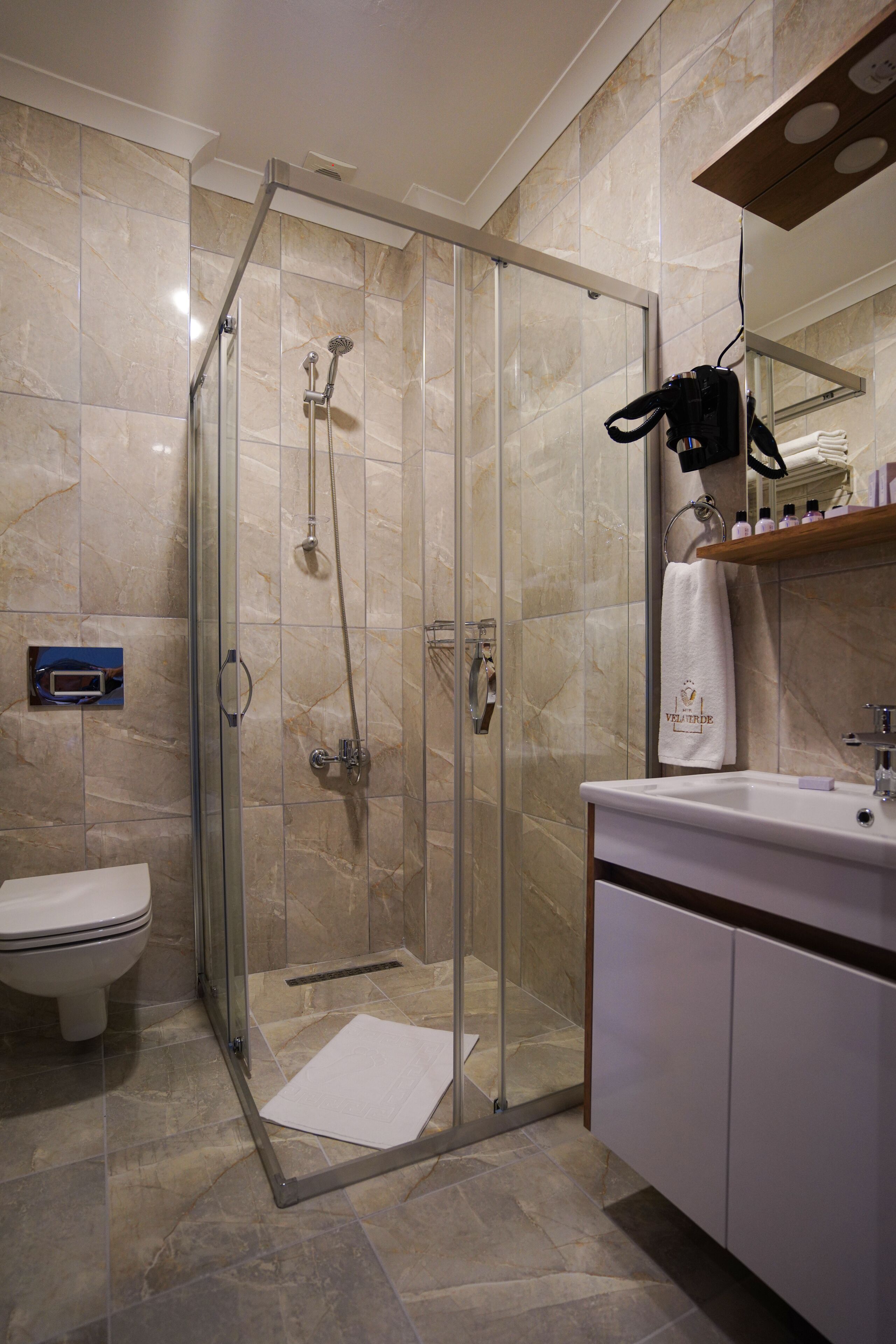 Un baño moderno con ducha de vidrio, un lavamanos blanco y suelo de baldosas de mármol.